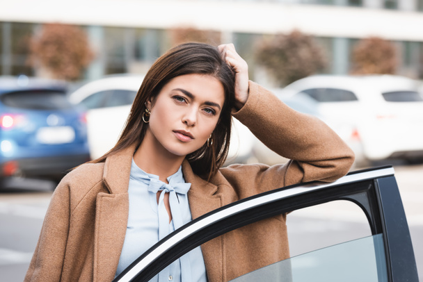dreamy young woman looking at camera while leaning on car door  - Fotografie, Obrázek