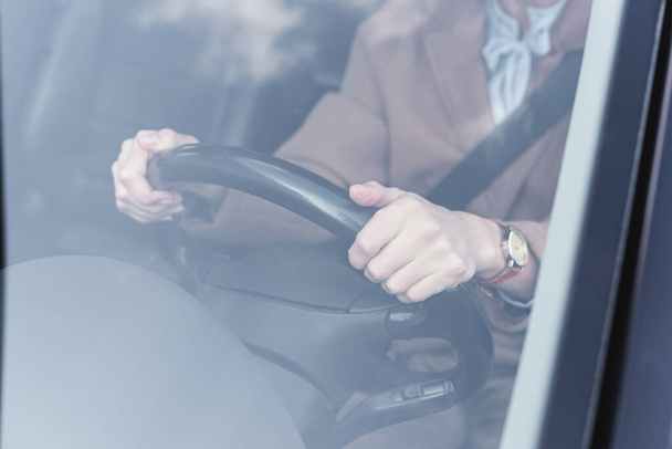 cropped view of woman holding steering wheel while driving car on blurred foreground - Foto, Imagem