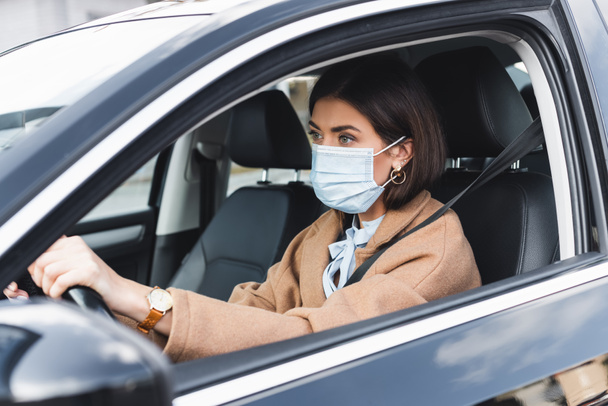 前景に車を走らせながら前を見ている医療用マスクの若い女性 - 写真・画像