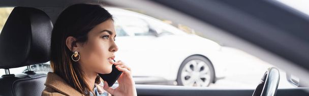 vista lateral de la mujer joven hablando en el teléfono inteligente mientras conduce el coche en primer plano borroso - Foto, imagen