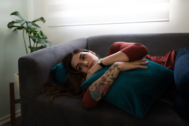 Latin young woman lying on the couch and hugging a pillow. Woman in his 20s looking sad and depressed - Photo, image