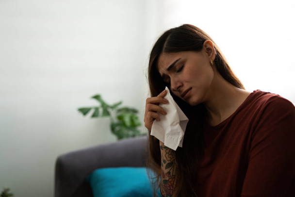 Särkynyt latino nuori nainen itkee ja pyyhkii kyyneleensä nenäliinalla. Nainen hänen 20s etsivät surullinen ja masentunut istuu sohvalla  - Valokuva, kuva