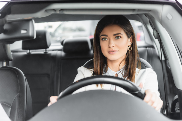 χαμογελαστή γυναίκα που κοιτάζει μπροστά ενώ οδηγεί αυτοκίνητο σε θολή πρώτο πλάνο - Φωτογραφία, εικόνα