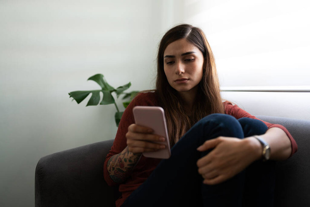 Krásná a nešťastná latinsky mladá žena pomocí svého smartphonu vypadá smutně a melancholicky - Fotografie, Obrázek