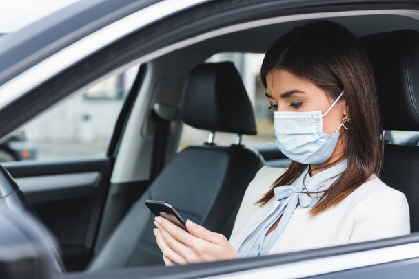 stílusos nő orvosi maszk chat mobiltelefon autóban elmosódott előtérben - Fotó, kép