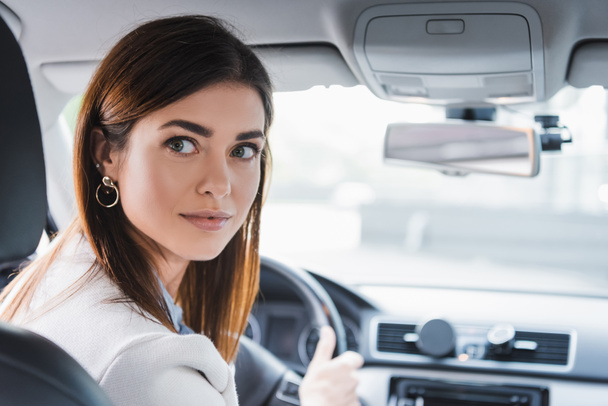 jeune femme regardant en arrière tout en conduisant une voiture sur fond flou - Photo, image