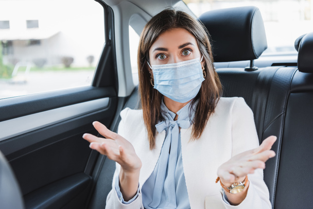 confused woman showing shrug gesture and looking at camera while sitting in car - Photo, Image