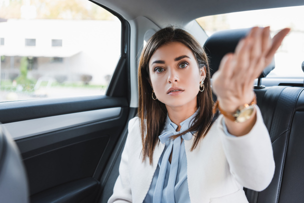elegant woman pointing with hand while sitting on back seat of car on blurred foreground - Photo, Image