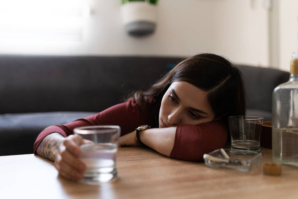Opilá hispánská mladá žena pije ve svém obýváku lihovou vodku. Latinská žena cítí osamělost a smutek  - Fotografie, Obrázek