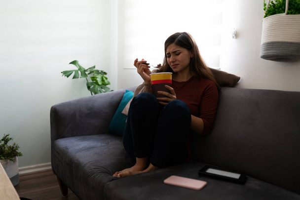 Triste et déprimée jeune femme latine manger de la crème glacée au chocolat dans le canapé en raison de sa solitude  - Photo, image