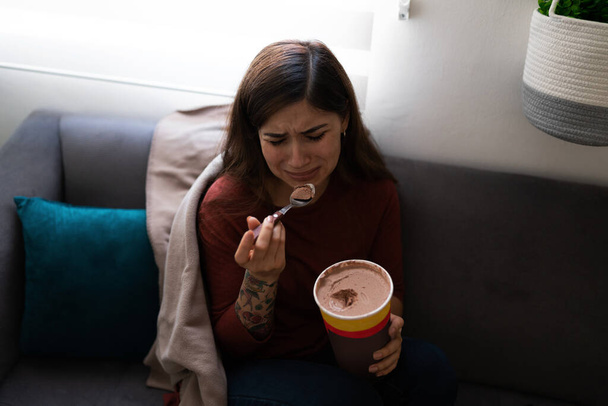 Depresivní a srdcervoucí mladá latinská žena, která jedla čokoládovou zmrzlinu, zatímco brečela na pohovce. Hispánka se cítí osamělá - Fotografie, Obrázek