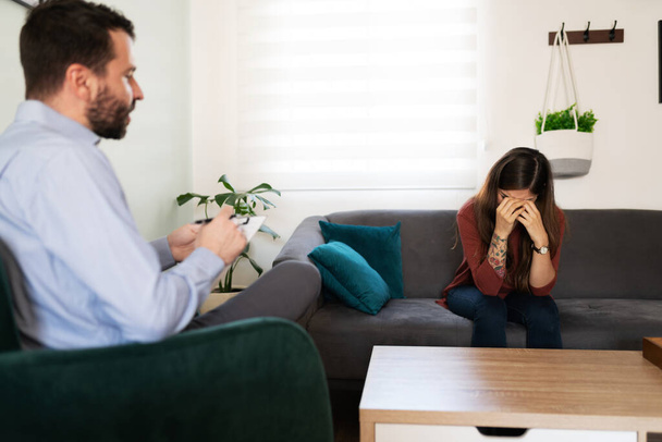 Hispanic woman in her 20s crying and hiding her face during a therapy session with her male psychiatrist  - Photo, Image