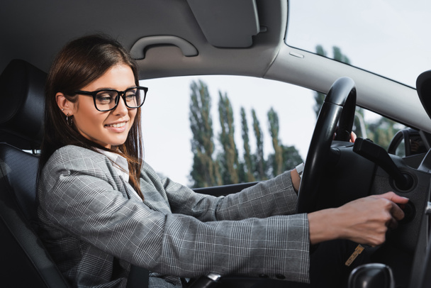 Gözlüklü mutlu iş kadını arabayı çalıştırırken gülümsüyor. - Fotoğraf, Görsel