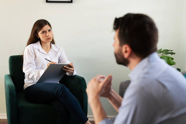 Kadın psikolog terapi seansı sırasında erkek hastasını dinliyor ve dikkatini veriyor. Stres ve sorunları olan yetişkin bir adam sorunları hakkında konuşuyor.  - Fotoğraf, Görsel