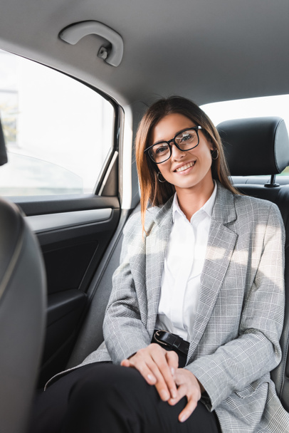feliz, elegante mujer de negocios sonriendo a la cámara mientras monta en coche en primer plano borrosa - Foto, imagen