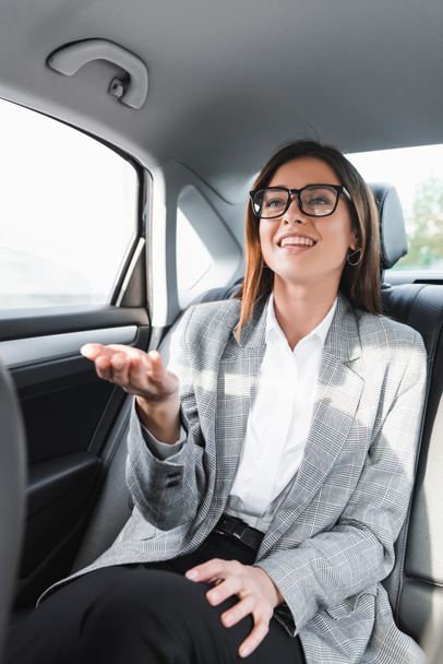 veselá podnikatelka v brýlích ukazuje rukou při jízdě v autě - Fotografie, Obrázek