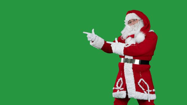 Święty Mikołaj na zielonym tle wskazuje dwoma palcami wskazującymi na puste miejsce na tekst. Przestrzeń kopiowania. - Zdjęcie, obraz