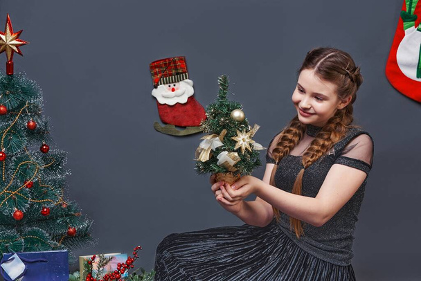 girl teenager with a small christmas tree. studio portrait gray background - Zdjęcie, obraz
