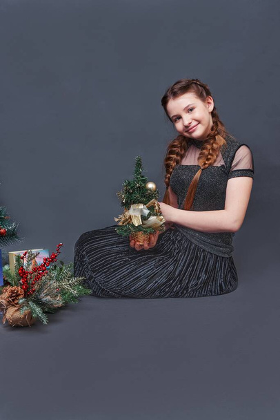girl teenager with a small christmas tree. studio portrait gray background - Zdjęcie, obraz