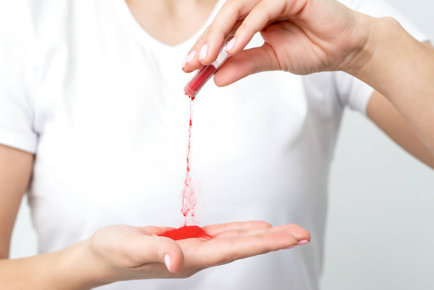 Closeup of manicure master pours red pigment nail powder from tube on her palm - Foto, Imagem