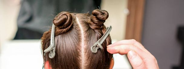 Vista trasera de la mano de la peluquera haciendo corte de pelo de mujer joven con clips de pelo en su peluquería - Foto, imagen