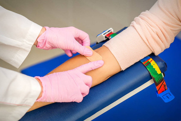 病院内の採血後、患者の腕に接着剤石膏を適用する看護師の手の閉じる - 写真・画像