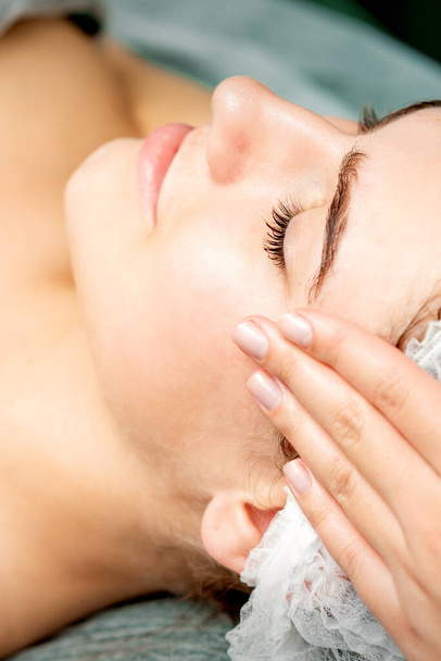 Young woman getting facial massage with closed eyes by beautician in beauty salon - Photo, image