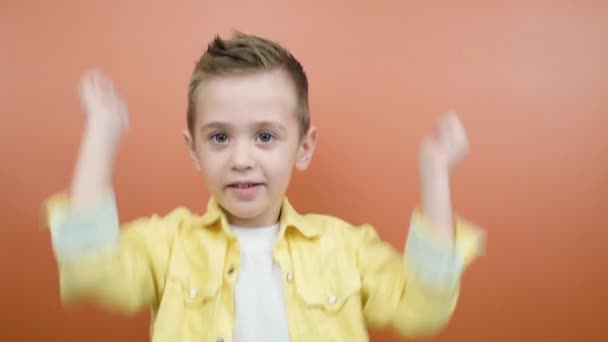 Petit garçon heureux amusant enfant 4-5 ans en chemise jaune posant les poings serrés faire geste gagnant dire Oui isolé sur fond orange studio. Concept de style de vie - Séquence, vidéo