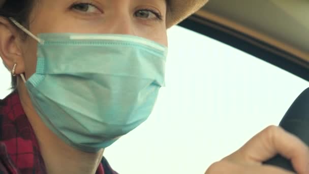 COVID-19の普及を防ぐため、医療用マスクを着用した車を運転する若い女性。車の中で顔のマスクを持つ女性の運転は、ウイルスのインフルエンザから保護する - 映像、動画