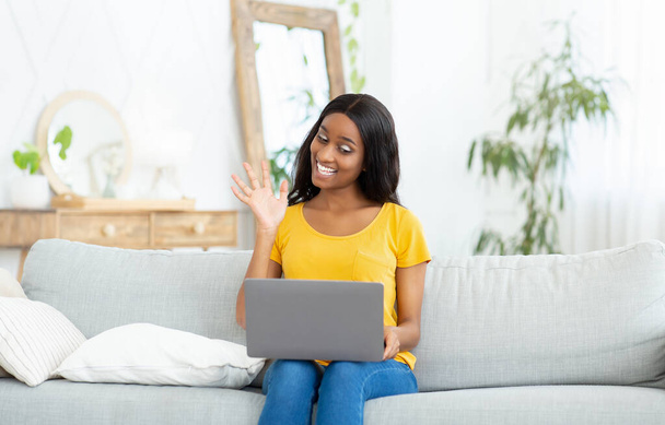 Communicatie op afstand. Joyful zwarte vrouw met laptop praten met familie, vrienden of collega 's online van huis - Foto, afbeelding