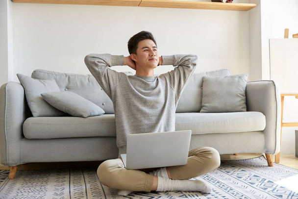 glücklich junge asiatische Geschäftsmann zu Hause sitzend auf Teppich arbeiten mit Laptop-Computer glücklich und lächelnd - Foto, Bild