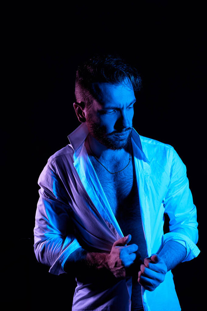 A brutal man on a dark background in a white shirt open at the chest.In the blue light. - Fotó, kép