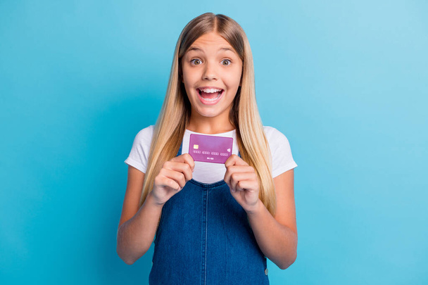 Portrait of surprised nice blond long hair girl showing credit card wear casual outfit isolated on pastel blue color background - Foto, afbeelding
