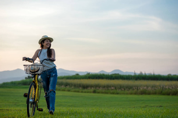 Smiling Asia woman with bicycling at the garden meadow in sunset near mountain background.  Lifestyle  Concept - Fotografie, Obrázek