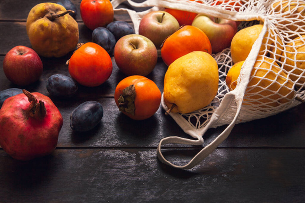 Varias frutas de otoño en una bolsa de malla sobre un fondo de madera oscura. - Foto, imagen