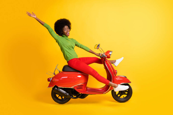Photo portrait of african american woman riding bike waving hand with spread legs open mouth isolated on vivid yellow colored background - 写真・画像