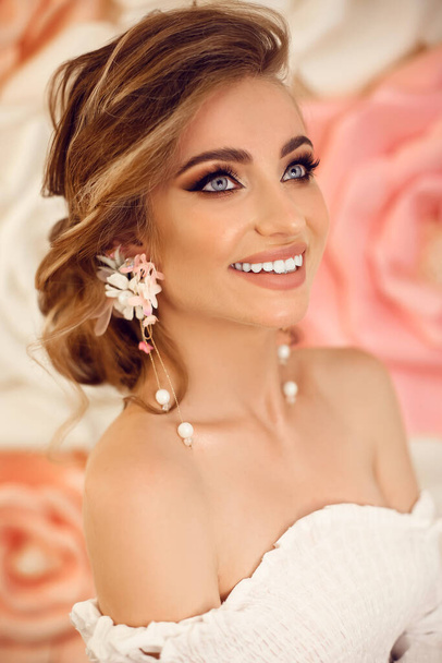 Beautiful young bride with makeup and fashion wedding hairstyle. Closeup portrait of young gorgeous woman over roses flowers. Studio shot. - Fotografie, Obrázek