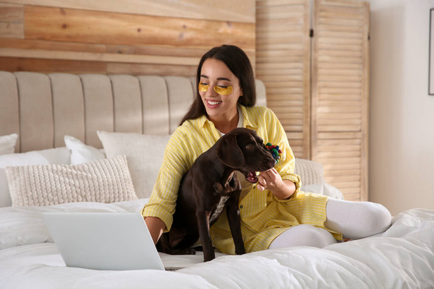 Young woman playing with her dog while working on laptop in bedroom. Home office concept - Fotografie, Obrázek
