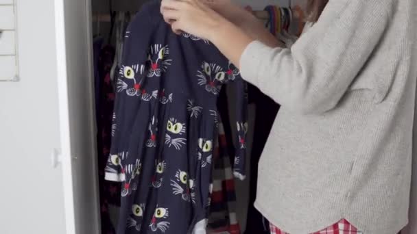 Äiti, kotiäiti, roikkuu mekkoja kaapissa hänen pieni tyttärensä kotona - Materiaali, video