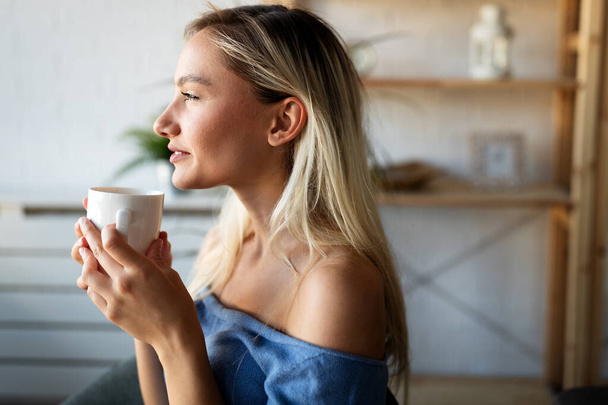 Beautiful young woman enjoying a cup of coffee, tea while relaxing at home. - Fotografie, Obrázek
