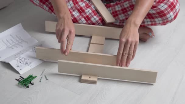 Een vrouw verbindt de delen van een houten plank en monteert deze met bouten en een schroevendraaier volgens de instructies - Video