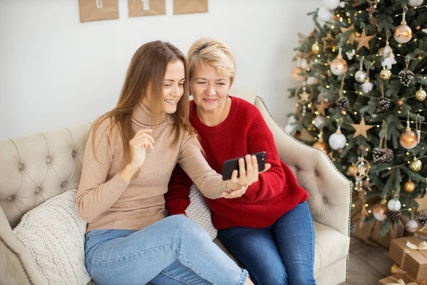 Lächelnde europäische blonde Mutter und reife Tochter benutzen Mobiltelefon für Videoanrufe mit Freunden und Eltern. - Foto, Bild