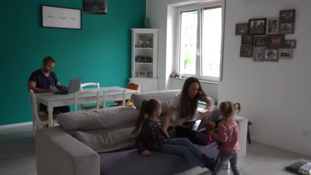ヨーロッパ、イタリア、ミラノ- Covid-19コロナウイルスのロックダウン流行中に自宅で家族のライフスタイル-リビングルームで遊んでいる子供たちと親のスマートワーキング-ロンバルディアレッドゾーン - 映像、動画