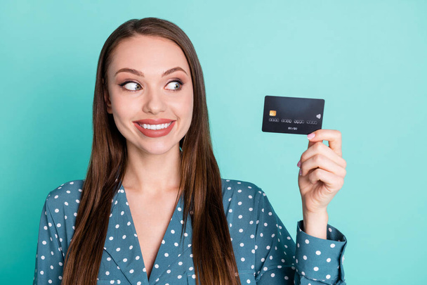 Portrait of positive cheerful girl hold look credit card wear polka-dot retro blouse isolated on teal color background - 写真・画像