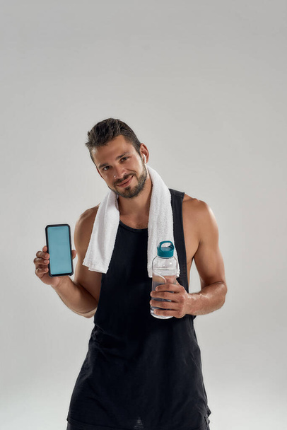 Happy young caucasian sportsman holding active smartphone - Zdjęcie, obraz