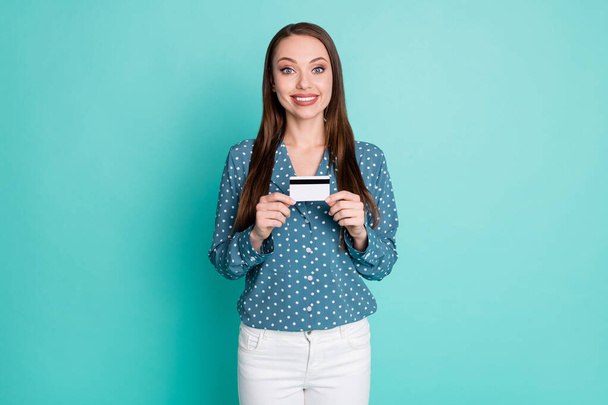 Photo of positive girl hold credit card wear blue blouse white pants isolated over teal color background - Foto, Bild