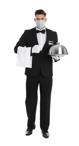 Waiter in medical face mask holding tray with lid on white background - Zdjęcie, obraz