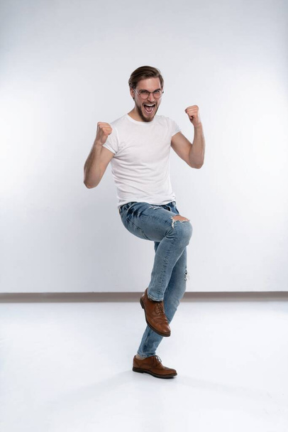 Happy winner. Happy young handsome man gesturing and keeping mouth open while standing against white background. - Foto, Bild