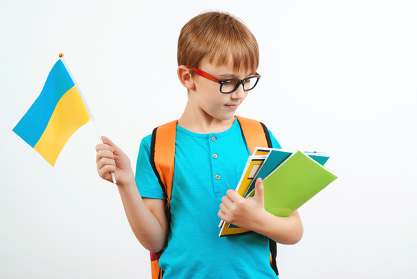 Az iskolás fiú ukrán nyelvet tanul. Aranyos fiú hátizsákkal ukrán zászlóval. Emberek, oktatás, tanulás és iskolai koncepció. Kis diák gazdaság könyvek, elszigetelt fehér. - Fotó, kép