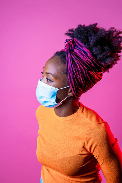 Portrait young black woman wearing surgical mak - Isolated woman on pink background using protective mask - healthcare, prevention, individual protection concept - Foto, immagini